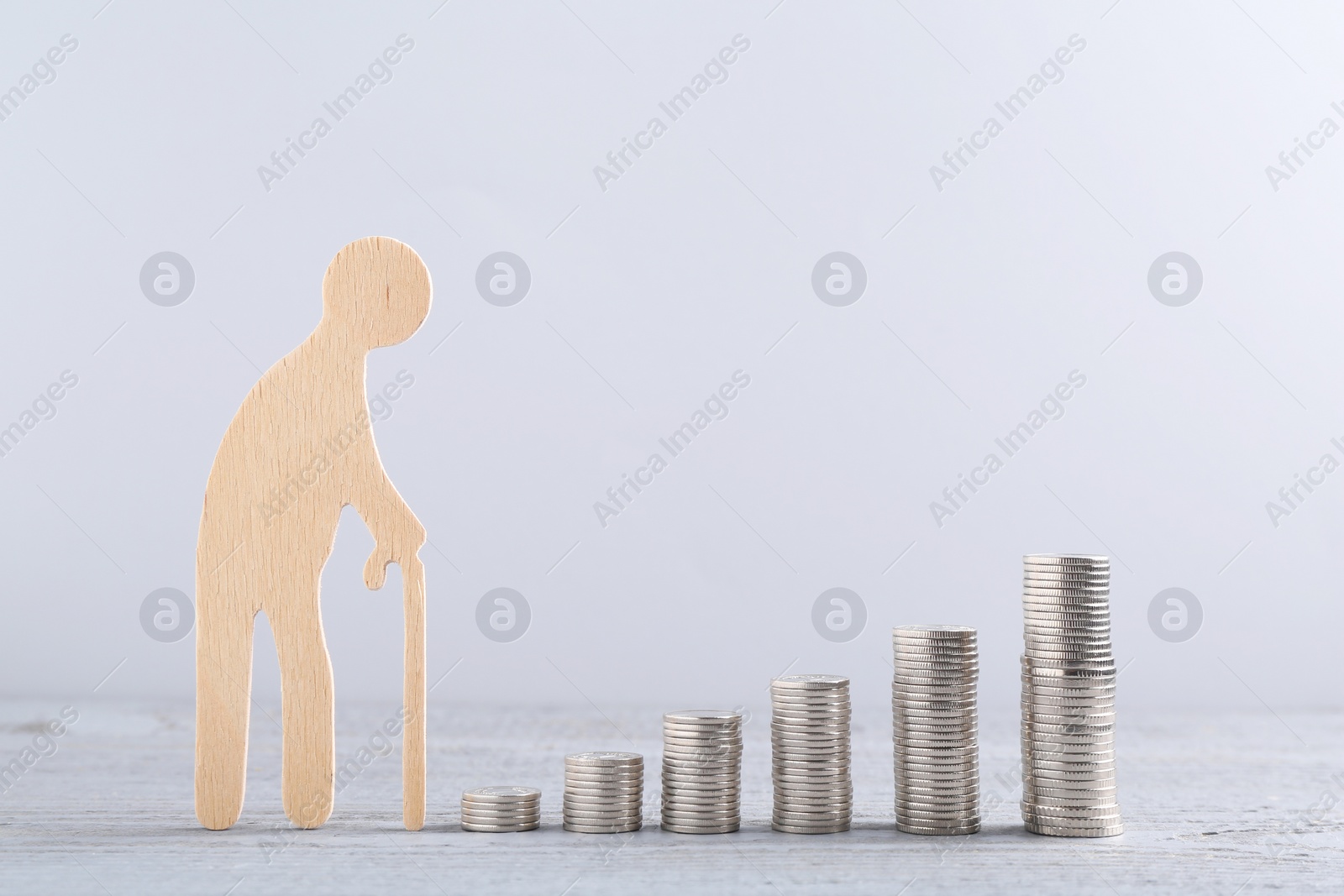 Photo of Pension savings. Figure of senior man and stacked coins on grey wooden table