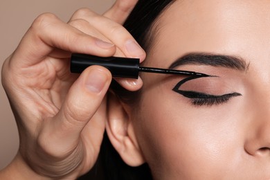 Artist applying black eyeliner onto woman's face on beige background, closeup
