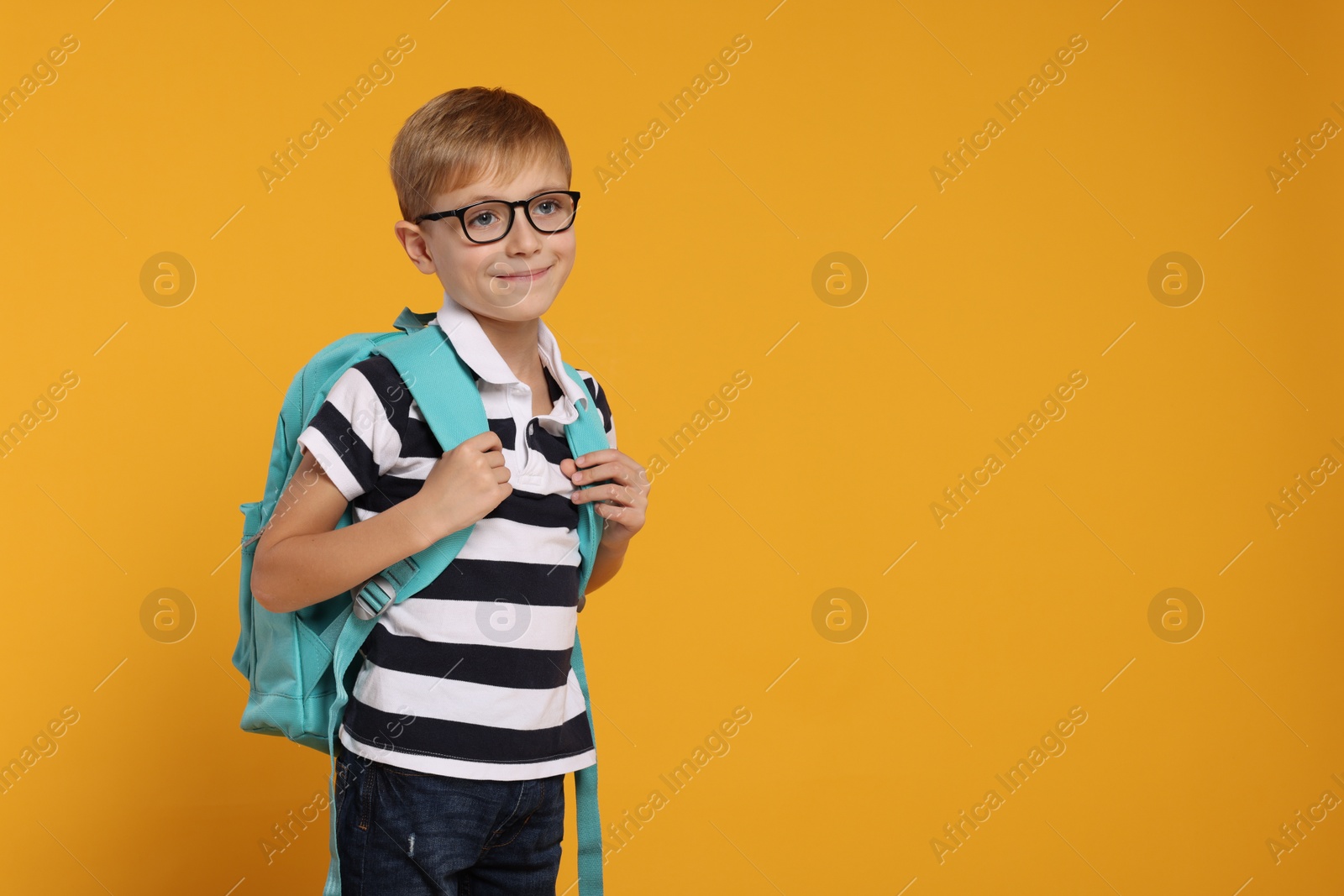 Photo of Happy schoolboy in glasses with backpack on orange background, space for text
