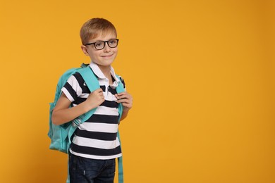 Happy schoolboy in glasses with backpack on orange background, space for text