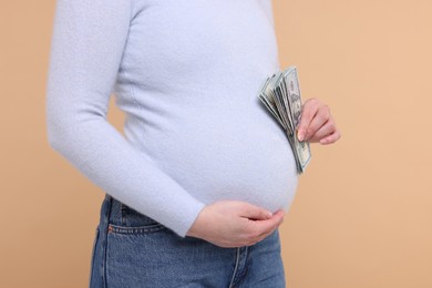 Surrogate mother. Pregnant woman with dollar banknotes on beige background, closeup