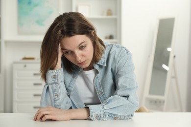 Photo of Sad young woman sitting at white table in room