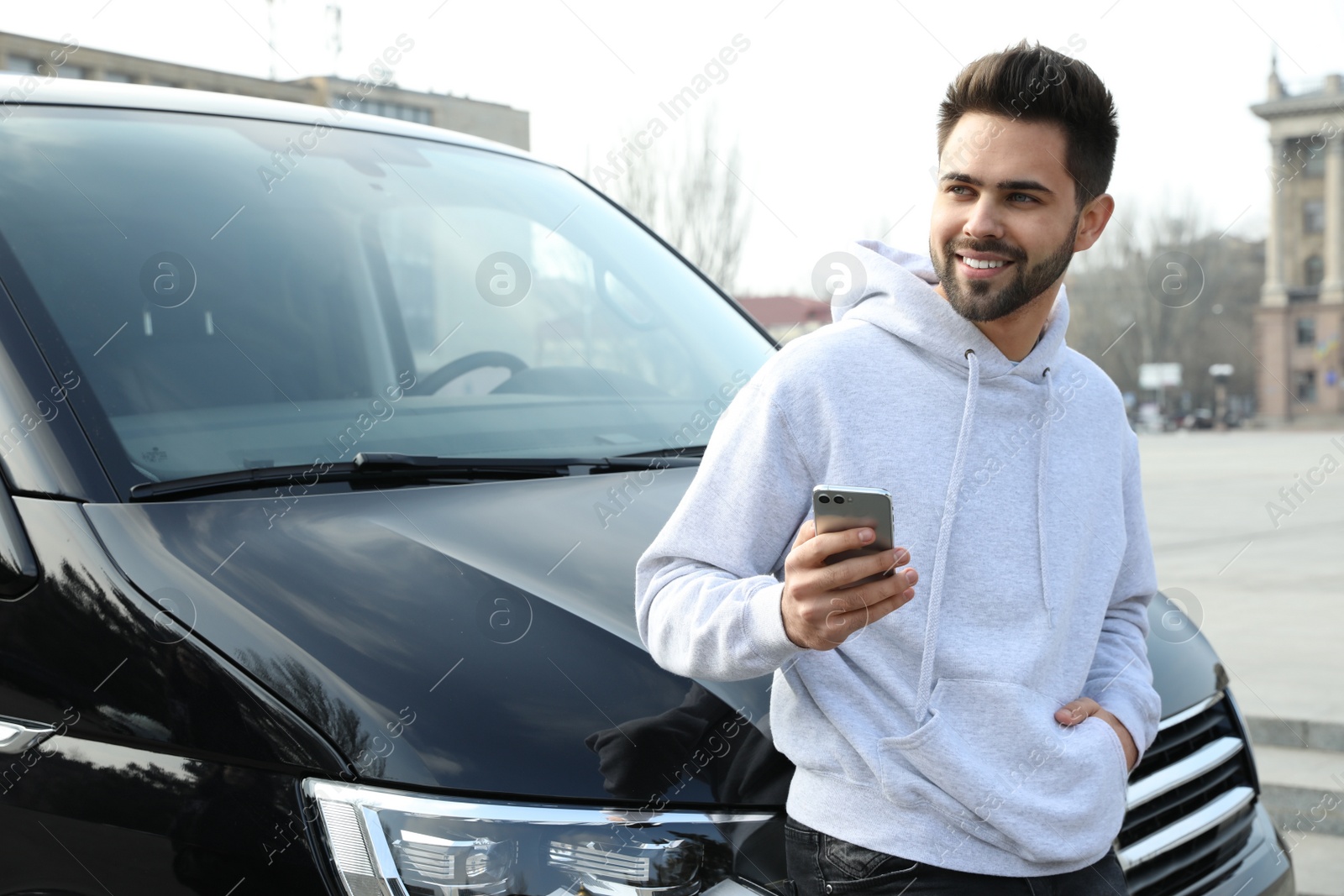 Photo of Handsome young man with smartphone near modern car outdoors