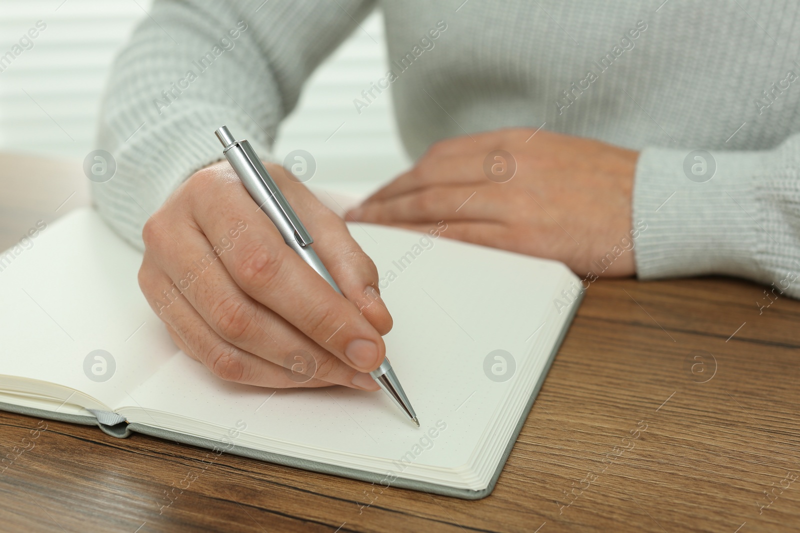 Photo of Man writing in notebook at wooden table, closeup