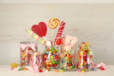 Photo of Jars with different delicious candies on beige wooden table