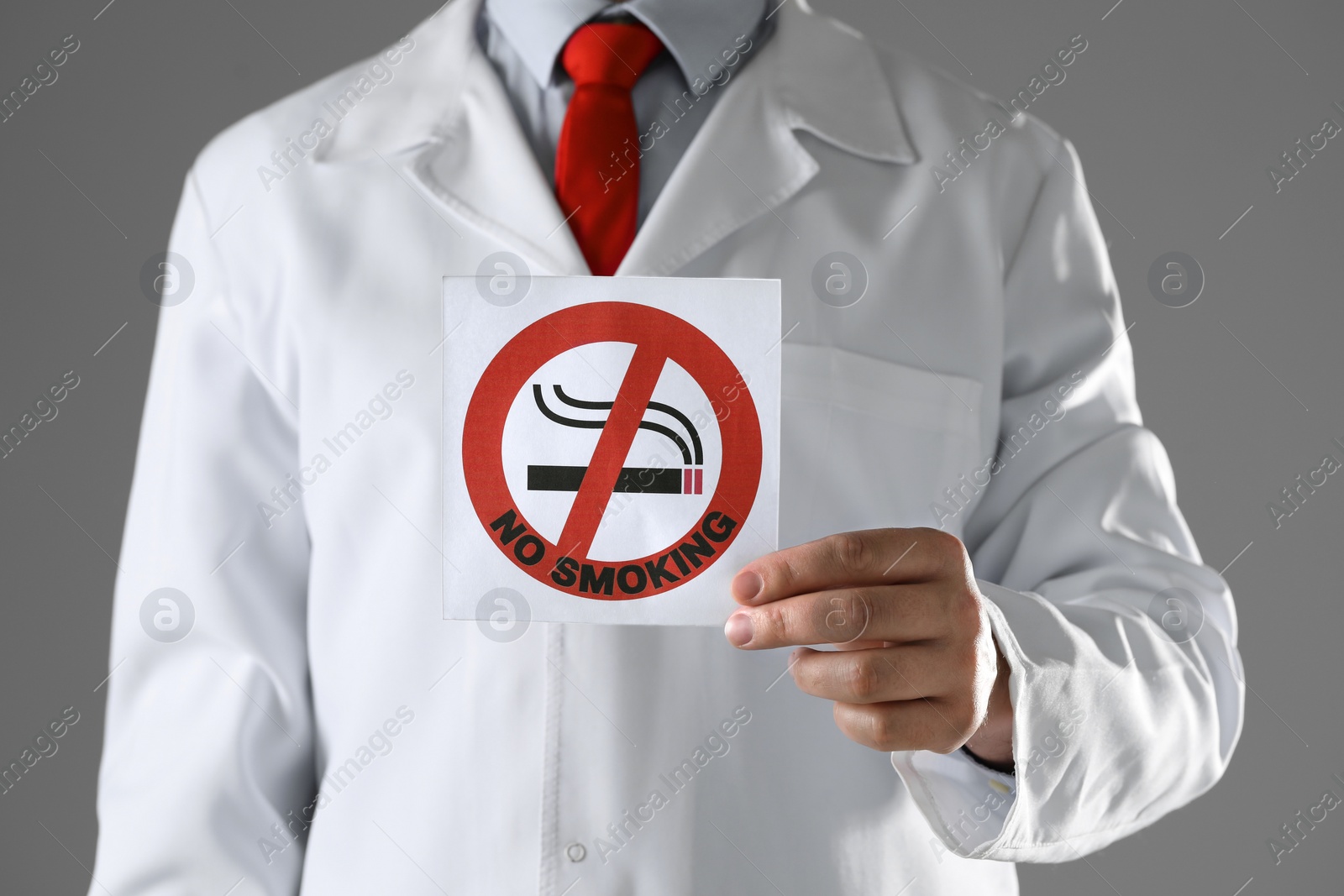 Photo of Doctor holding card with no smoking sign on gray background, closeup