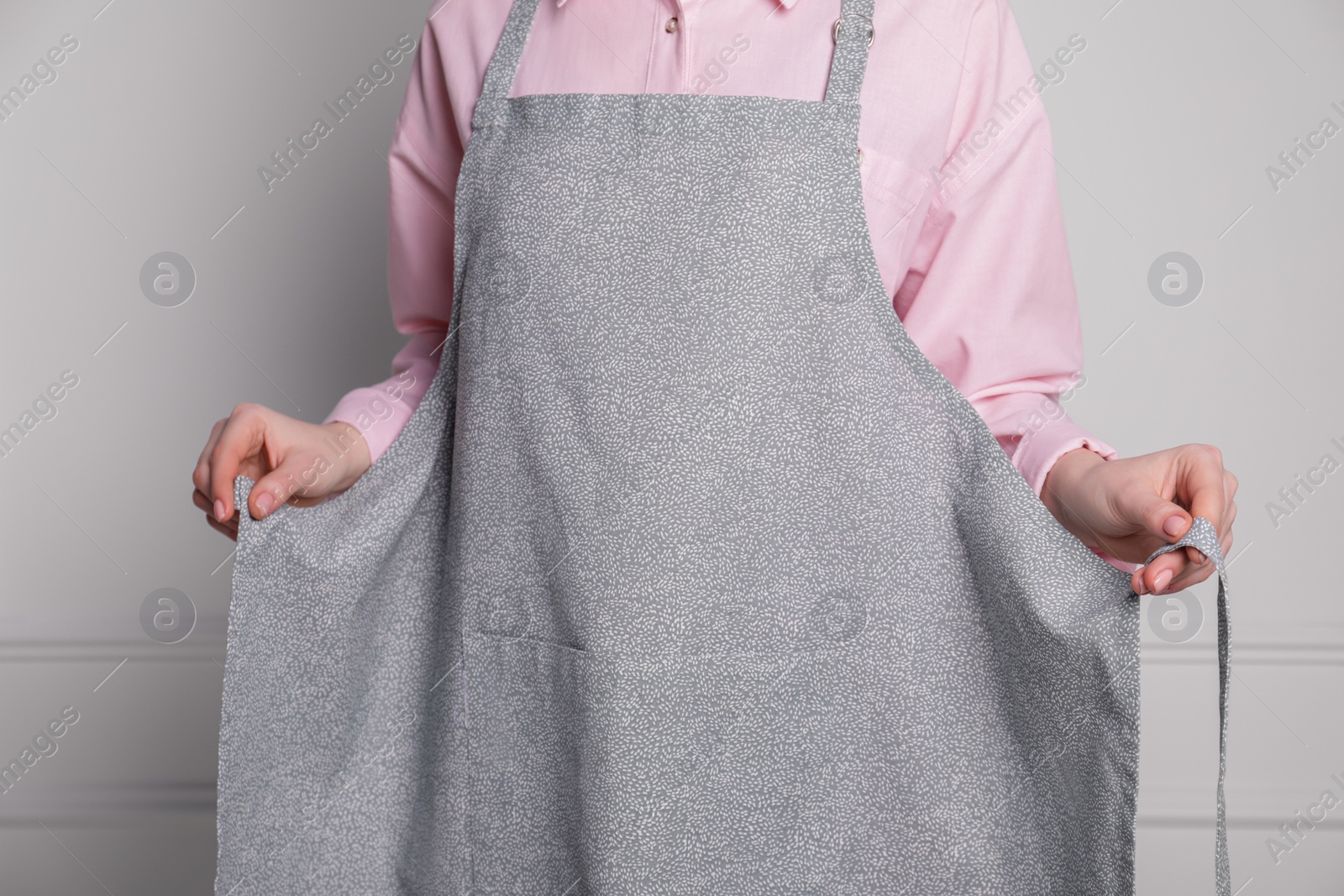 Photo of Woman putting on grey apron against white wall, closeup