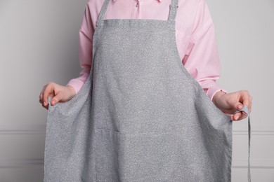 Photo of Woman putting on grey apron against white wall, closeup