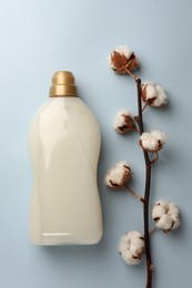 Photo of Bottle of fabric softener and branch with fluffy cotton flowers on light background, flat lay