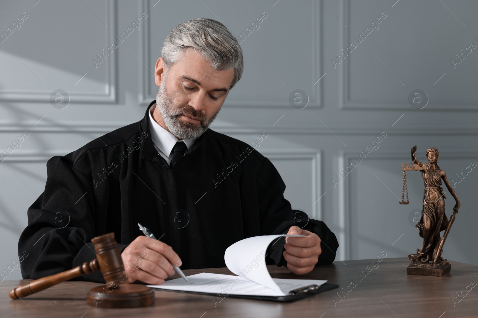 Photo of Judge with gavel writing in papers at wooden table indoors