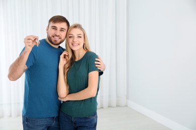 Happy young couple with key from their new house indoors, space for text