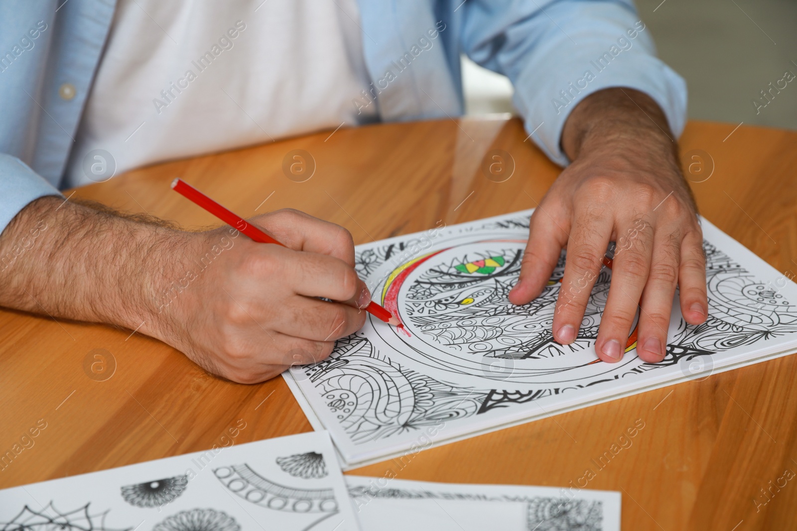 Photo of Man coloring antistress picture at table indoors, closeup