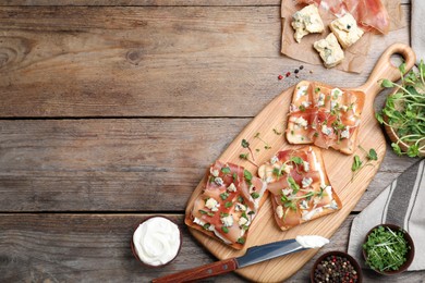 Photo of Delicious sandwiches with prosciutto, cheese and microgreens on wooden table, flat lay. Space for text