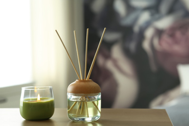 Photo of Aromatic reed air freshener and scented candle on table indoors