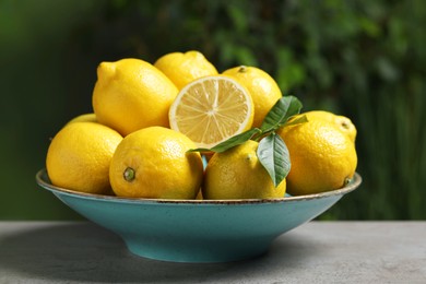 Photo of Fresh lemons and green leaves on grey table outdoors