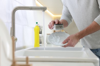 Man washing plate above sink in kitchen, closeup