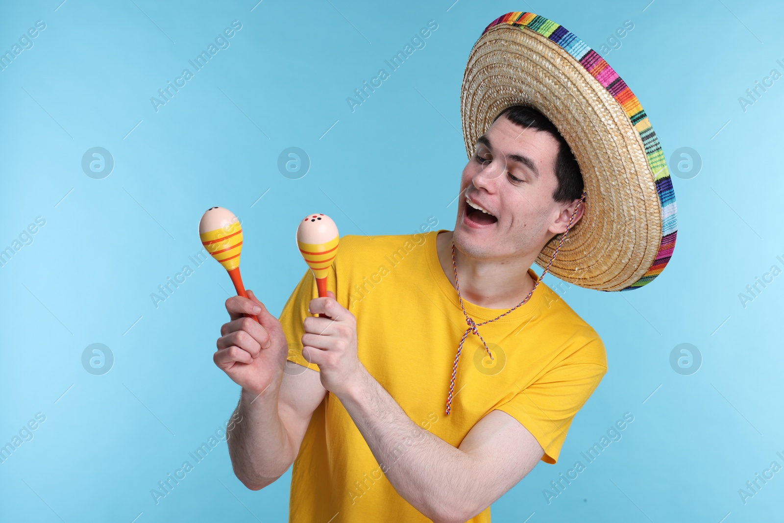 Photo of Young man in Mexican sombrero hat with maracas on light blue background