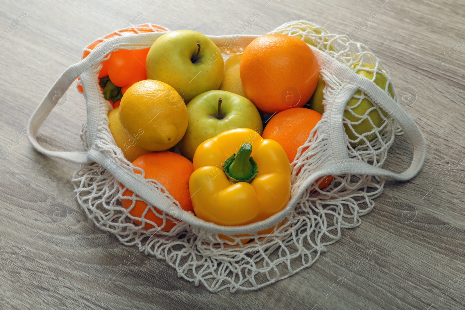 Photo of Net bag with vegetables and fruits on wooden table