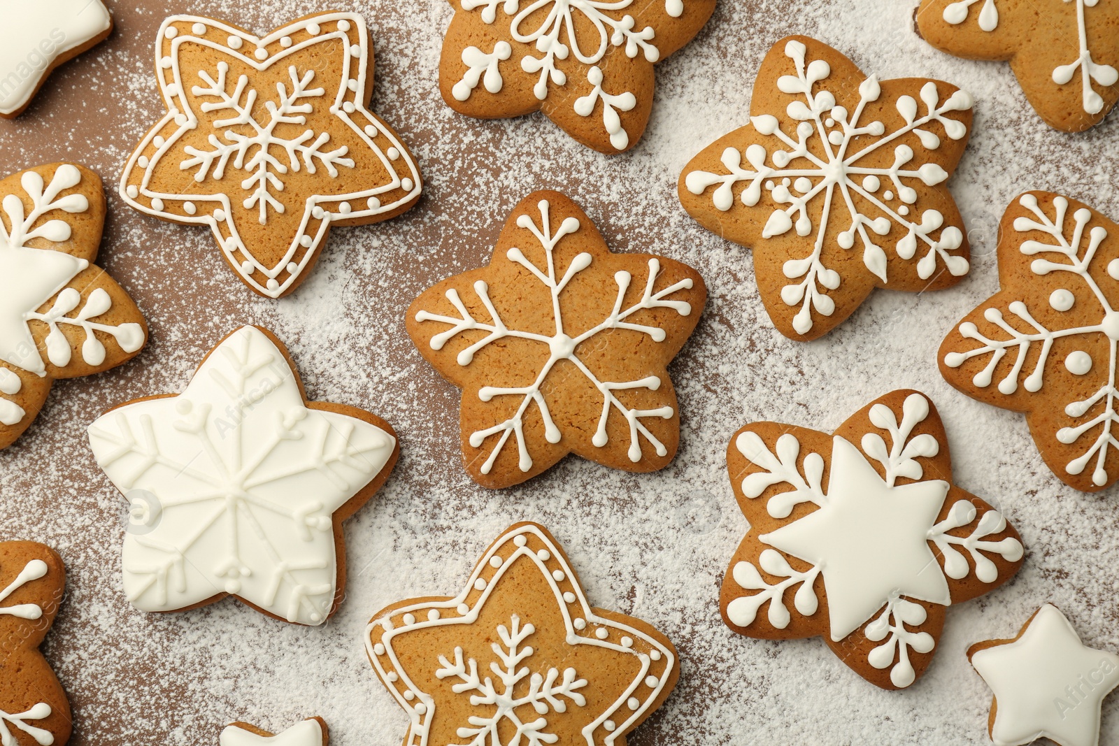 Photo of Tasty Christmas cookies with icing and powdered sugar on brown background, flat lay