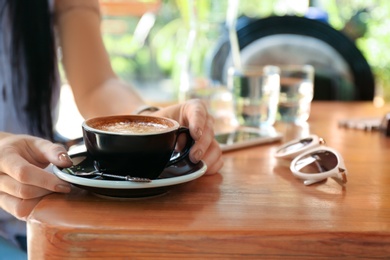 Woman with cup of fresh aromatic coffee at table, closeup