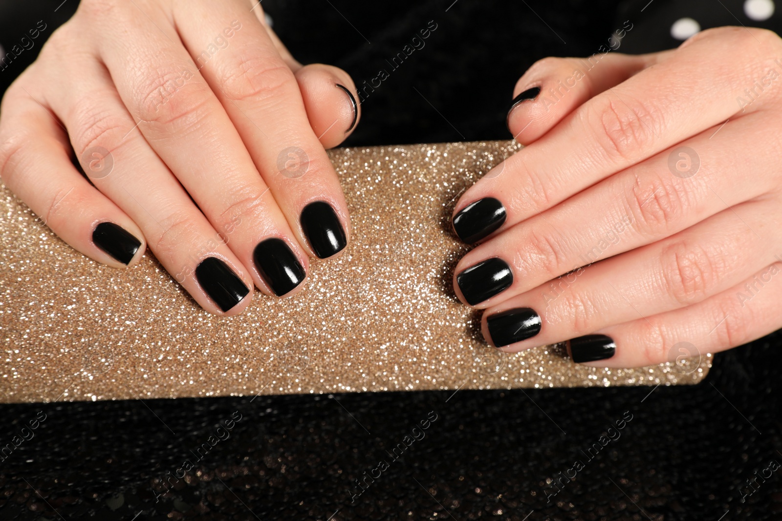 Photo of Woman showing black manicure on rolled shiny paper, closeup. Nail polish trends