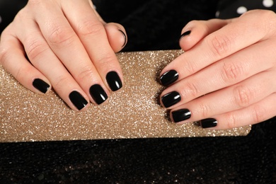 Photo of Woman showing black manicure on rolled shiny paper, closeup. Nail polish trends