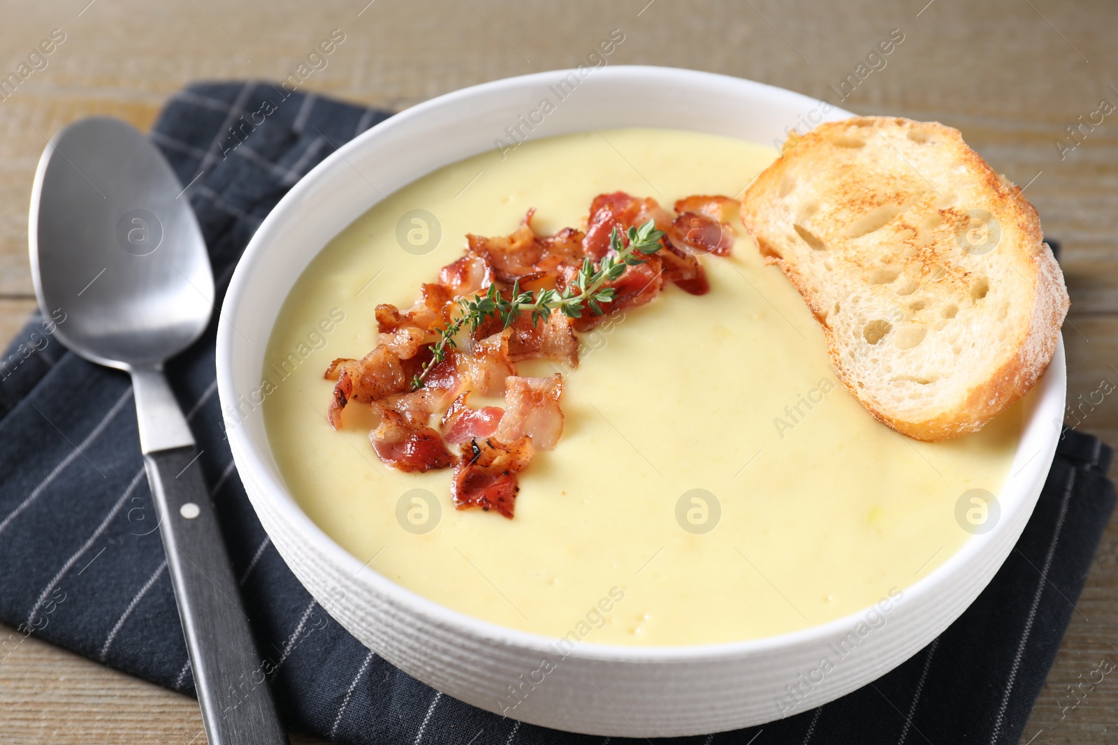 Photo of Tasty potato soup with bacon and rosemary in bowl served on wooden table