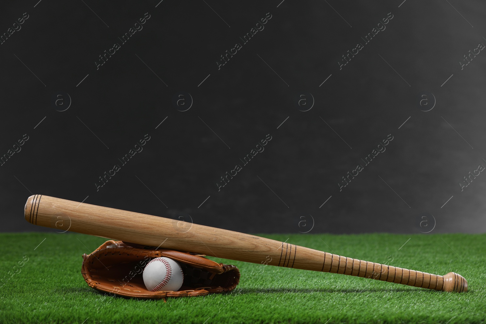 Photo of Baseball bat, leather glove and ball on green grass against dark background. Space for text