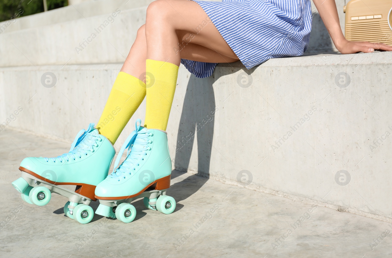 Photo of Young woman with vintage roller skates and radio sitting on stone stairs, closeup view