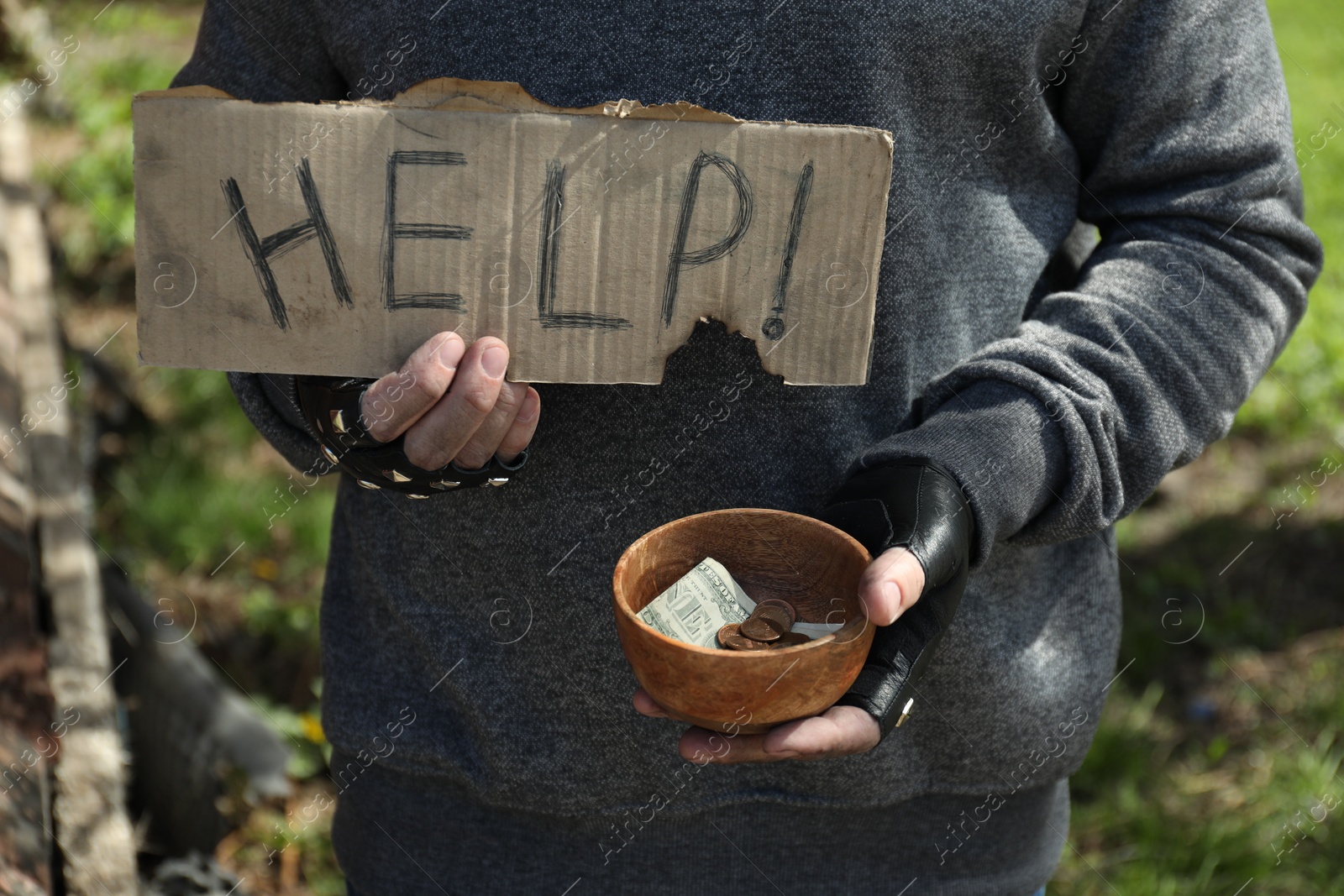 Photo of Poor homeless man holding help sign and bowl with donations outdoors, closeup