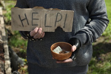 Poor homeless man holding help sign and bowl with donations outdoors, closeup