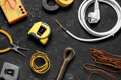 Photo of Different electrical wires and tools on black textured table, flat lay