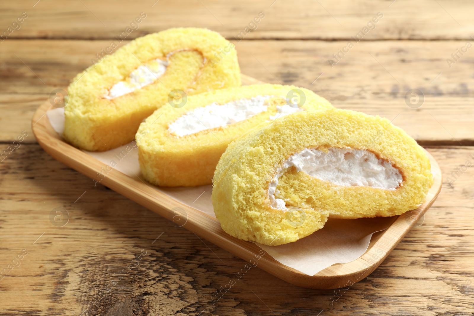 Photo of Delicious cake roll with cream filling on wooden table, closeup