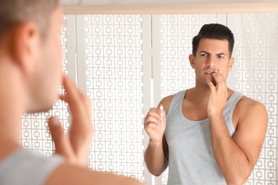 Emotional man with herpes applying cream on lips in front of mirror at home