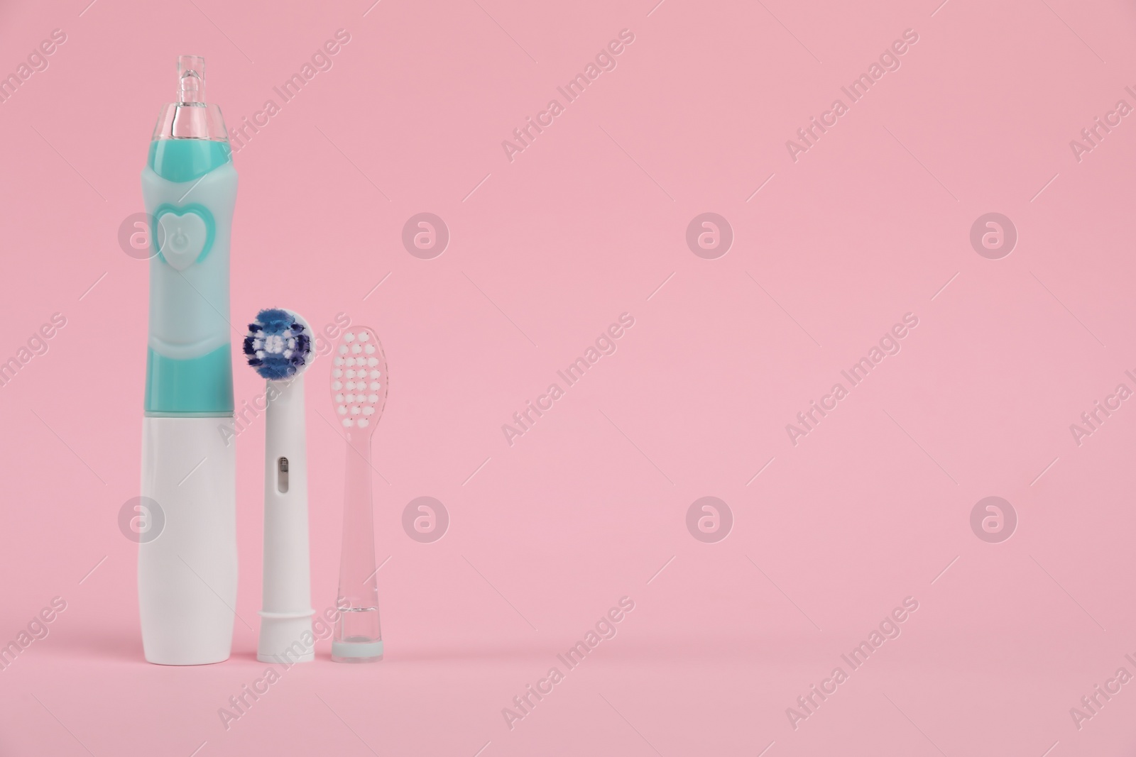 Photo of Electric toothbrush and replacement brush heads on pink background, space for text