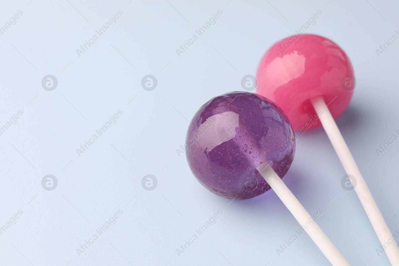 Photo of Tasty lollipops on light blue background, closeup. Space for text