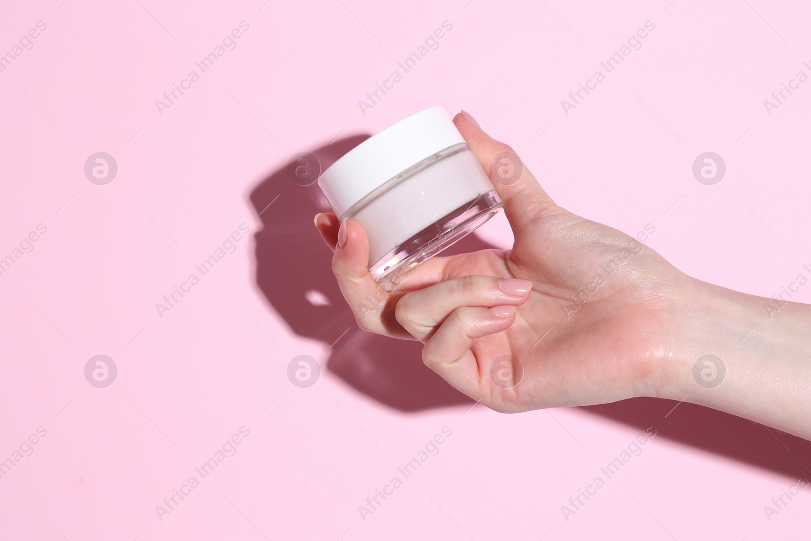 Photo of Woman holding jar of cream on pink background, closeup