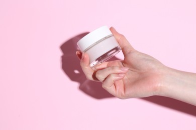 Woman holding jar of cream on pink background, closeup