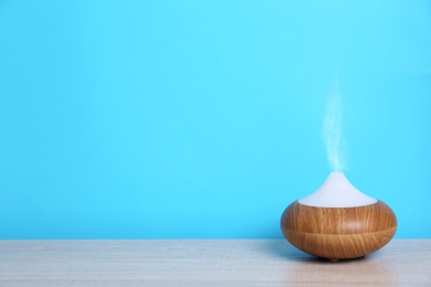 Photo of Essential oils diffuser on table near blue wall. Space for text