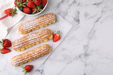 Delicious eclairs filled with cream and strawberries on white marble table, top view. Space for text