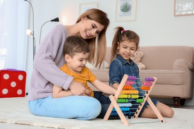 Nanny and little children playing with counting frame at home