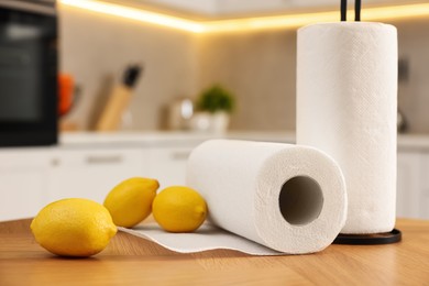 Photo of Rolls of white paper towels and lemons on wooden table in kitchen, closeup. Space for text