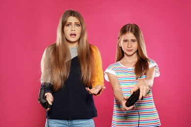 Young woman and teenage girl playing video games with controllers on color background