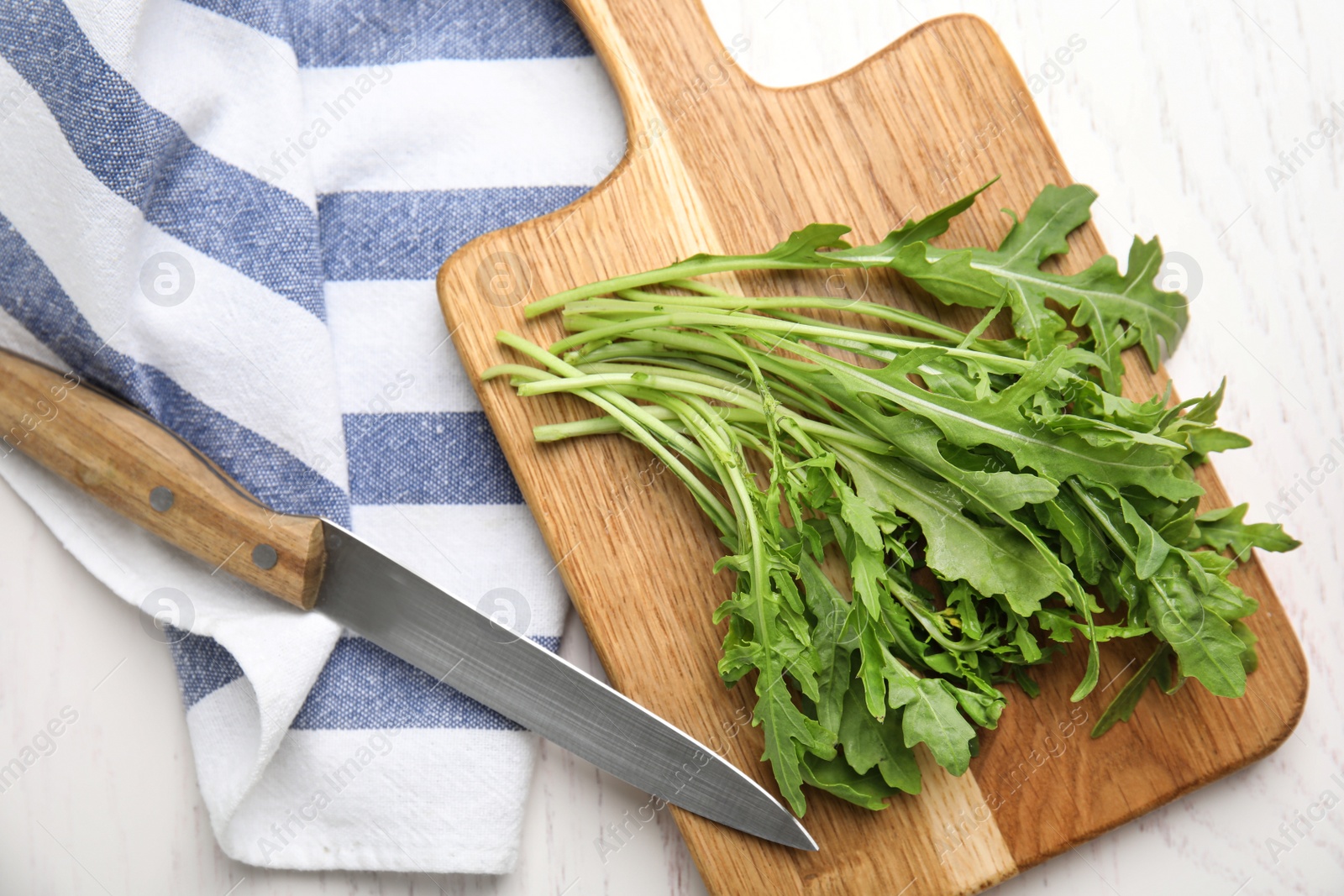 Photo of Fresh arugula, cutting board and knife on white wooden table, flat lay