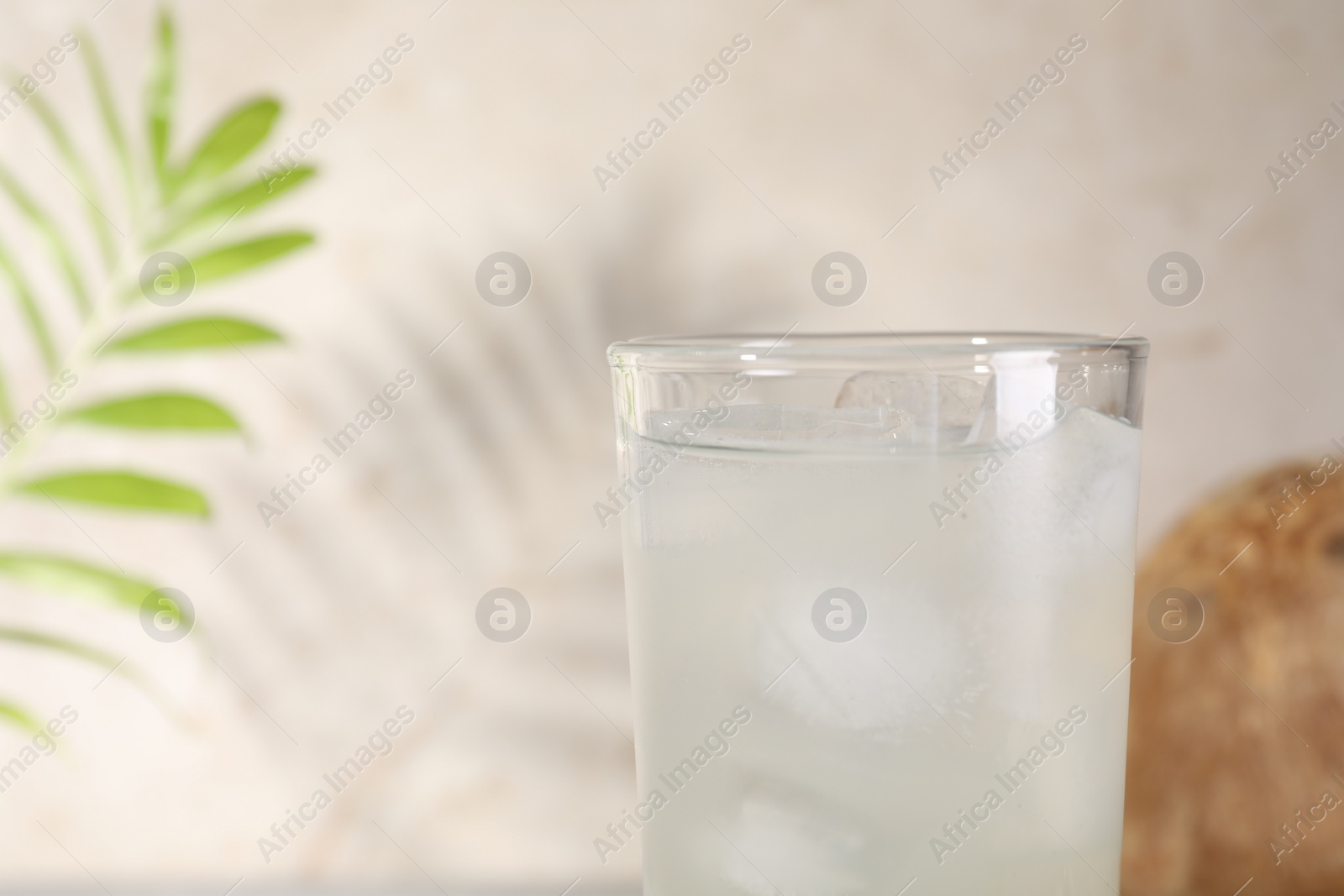 Photo of Glass of coconut water and ice cubes on light background, closeup. Space for text