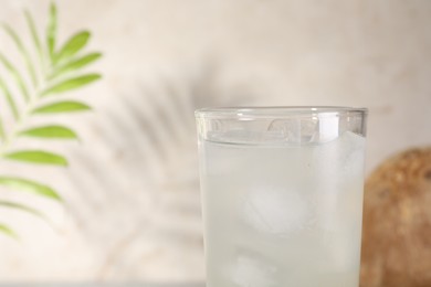 Photo of Glass of coconut water and ice cubes on light background, closeup. Space for text