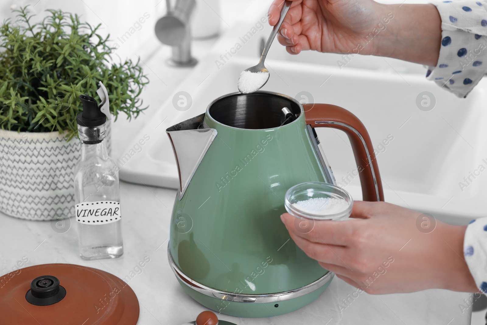 Photo of Woman adding baking soda into electric kettle in kitchen, closeup