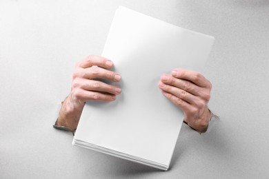 Photo of Man holding sheets of paper through holes in white paper, closeup. Mockup for design