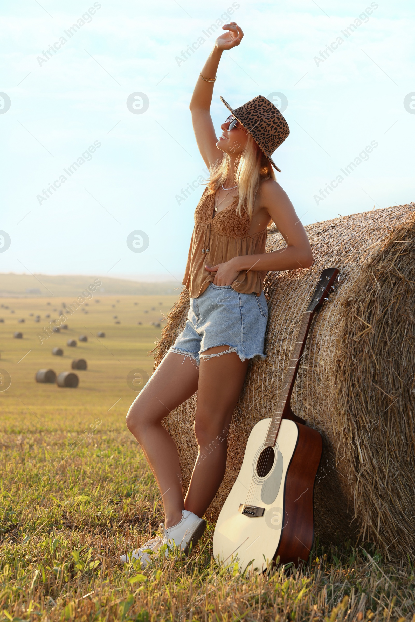 Photo of Happy hippie woman with guitar near hay bale in field