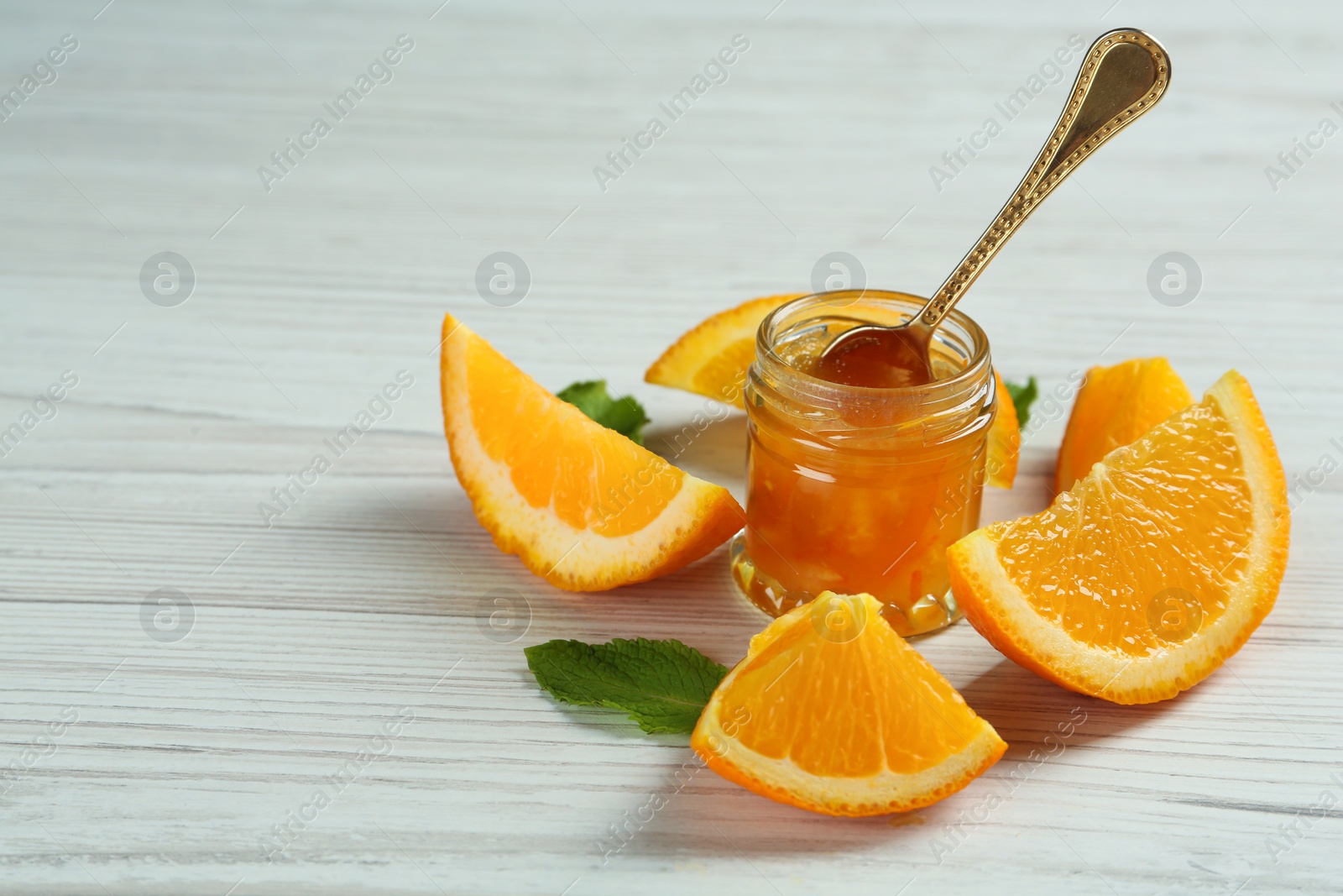 Photo of Jar of sweet orange jam and mint on white wooden table, space for text